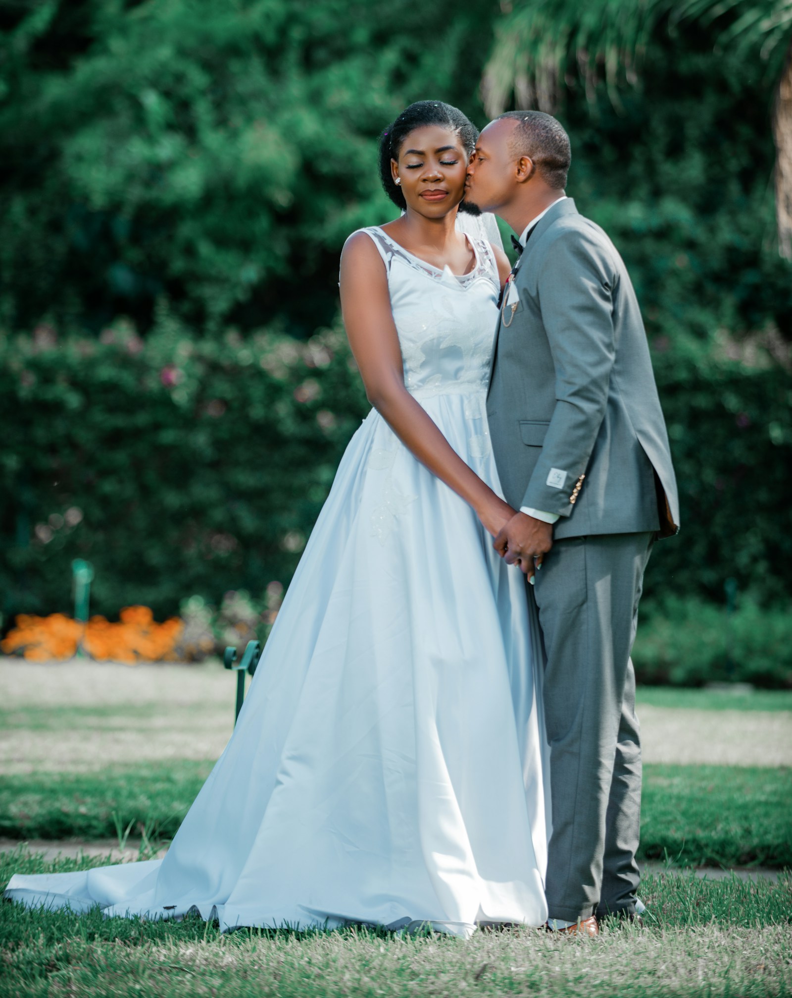 A bride and groom in a garden, the groom kissing her cheek
